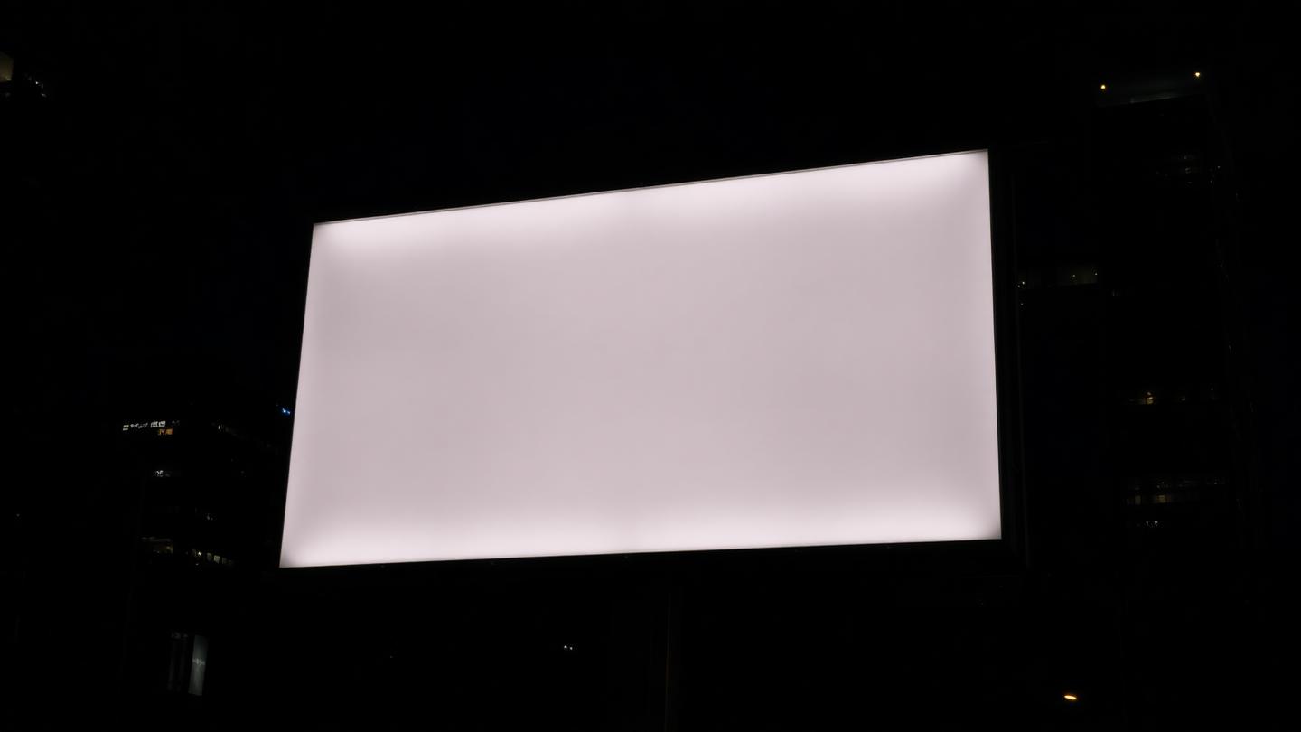 Backlit urban billboard at night, blank surface against a skyline background.